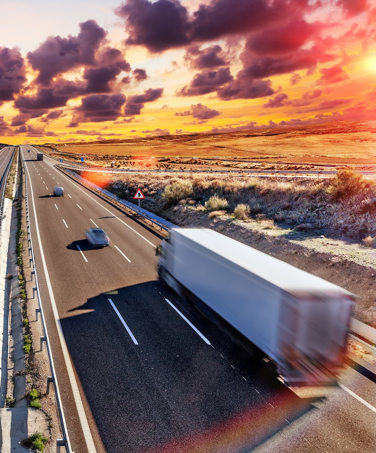 semi-truck and vehicles driving down highway at sunset