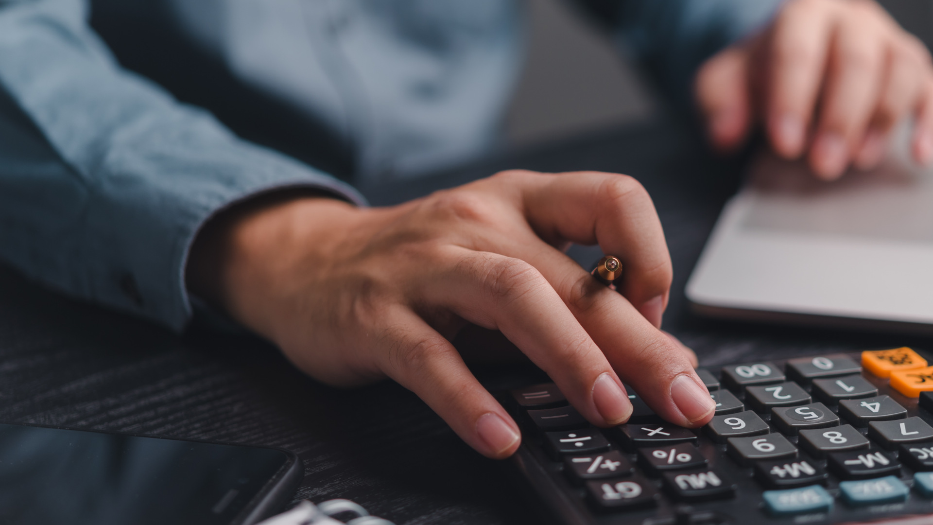 Person using calculator at desk with laptop and smartphone